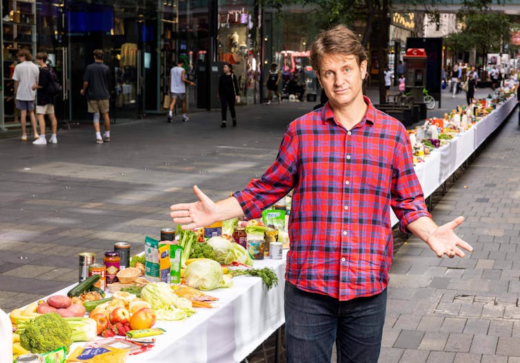 Craig Reucassel stands alongside a 50m long table covered in food, which is the amount one family wastes in a year