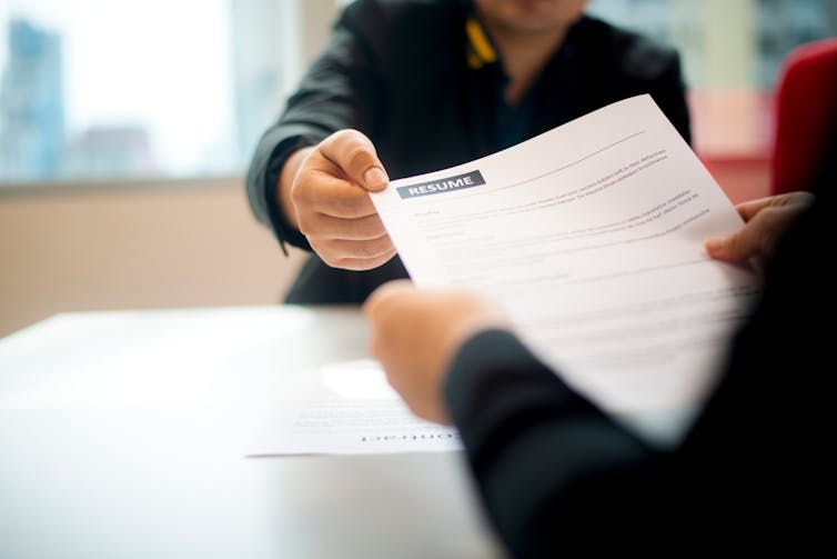 Man handing document across a desk to another person