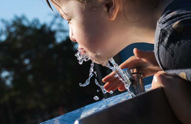 child drinks from bubbler water fountain
