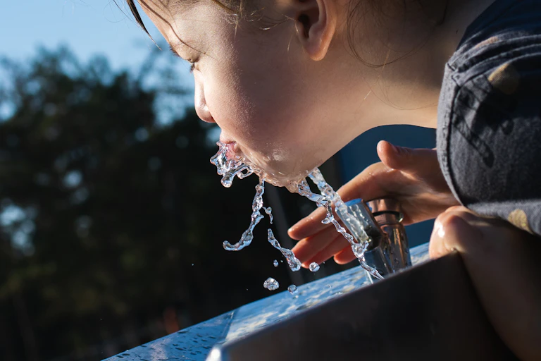 child drinks from bubbler water fountain