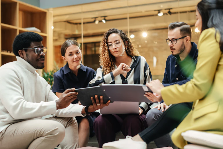 Group of people in casual clothes at work, looking at a laptop and notebook.