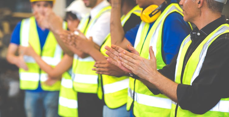 Line of people in high-vis vests, clapping.