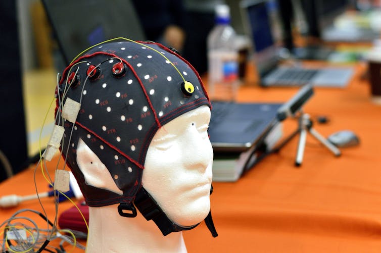 A black cap covered in wires fitted over a mannequin's head.