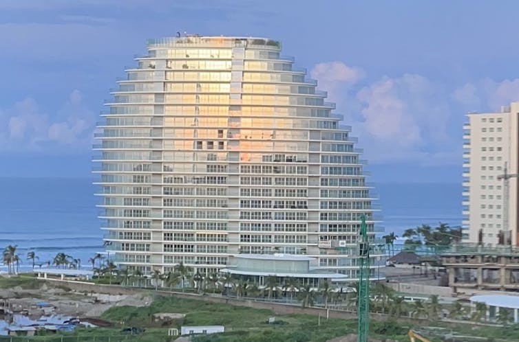 A large glass tower with sloping sides, like a sliced egg, reflects the sunrise with the Pacific Ocean looking placid in the background.