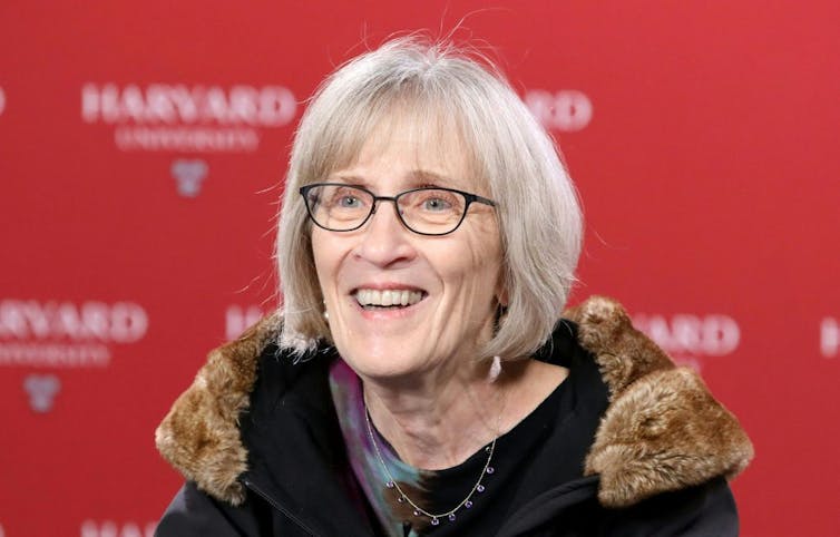 Woman with white hair and glasses smiling.