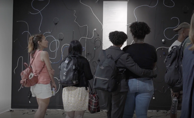 People seen looking at an installation of cords against a black wall.
