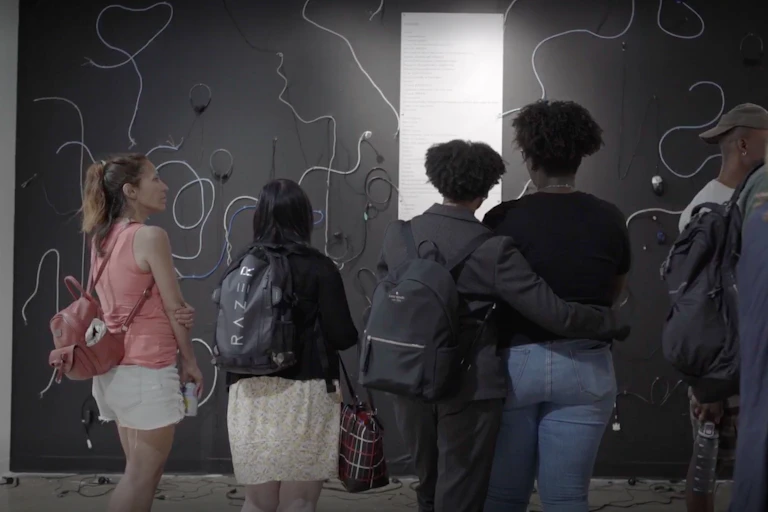 People seen looking at an installation of cords against a black wall.