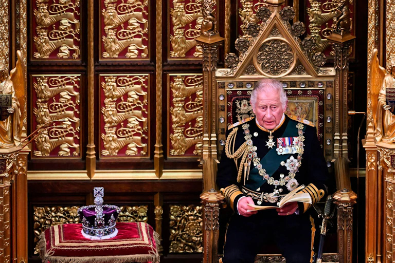 King Charles III, then Prince of Wales, sitting in uniform in an ornate, gilded chair, with the imperial state crown on a cushion beside him