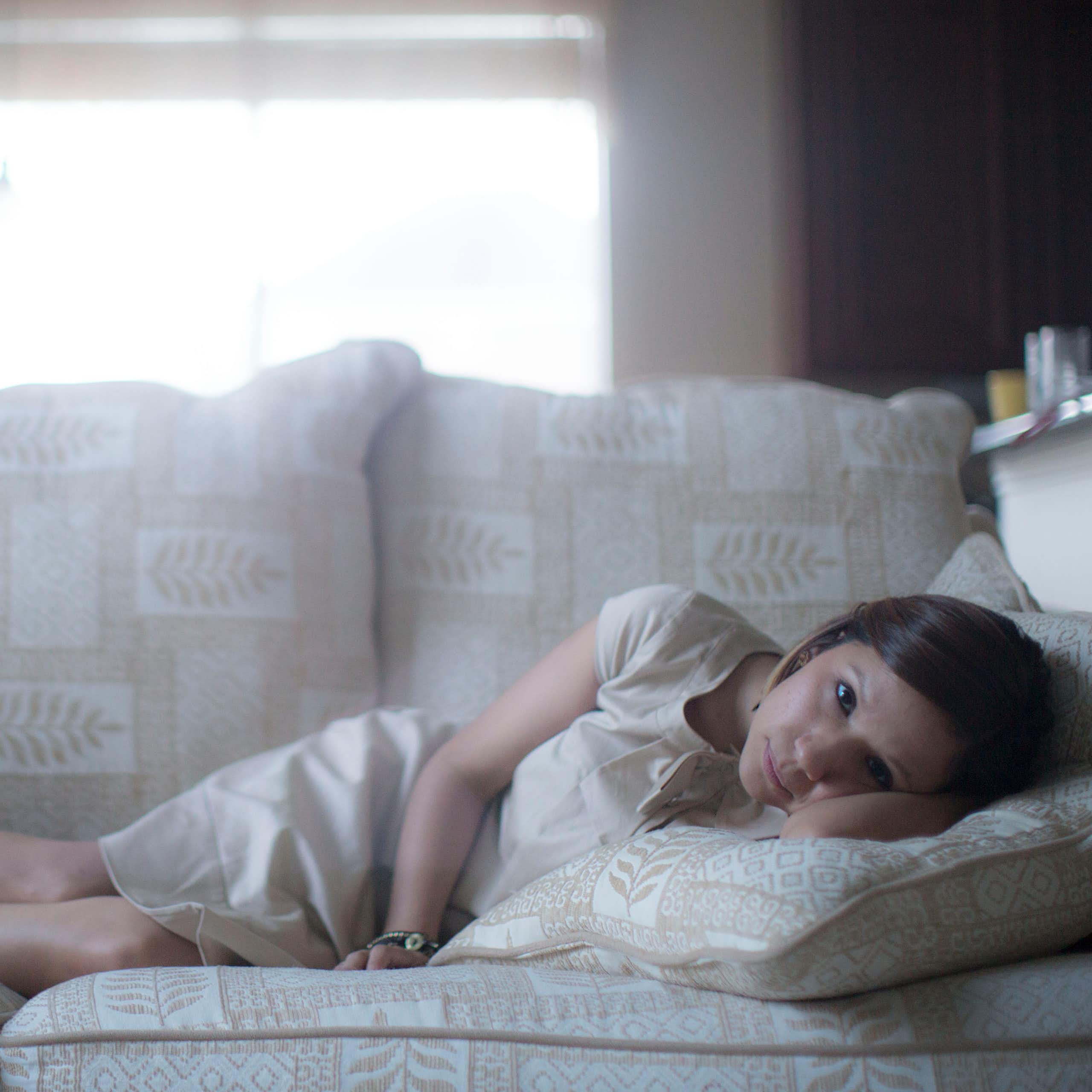 Mujer joven tumbada en un sofá blanco mirando directamente a la cámara.