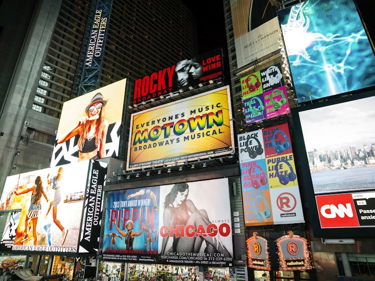 The names of different musicals are illuminated by neon signs.