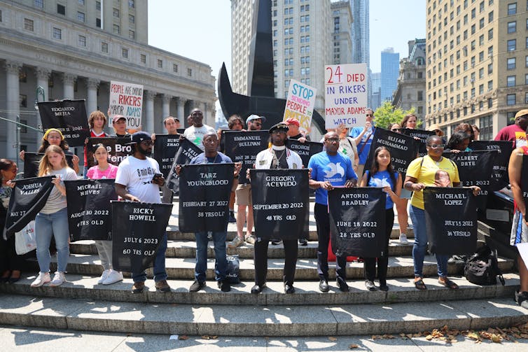 A group of people stand on a staircase while holding posters that have the names of people written in large letters.