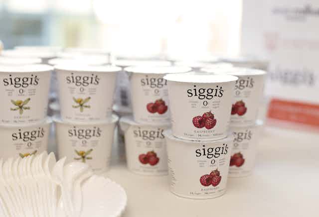 Rows of raspberry and vanilla yogurt containers stacked two high, with plastic spoons in the foreground.