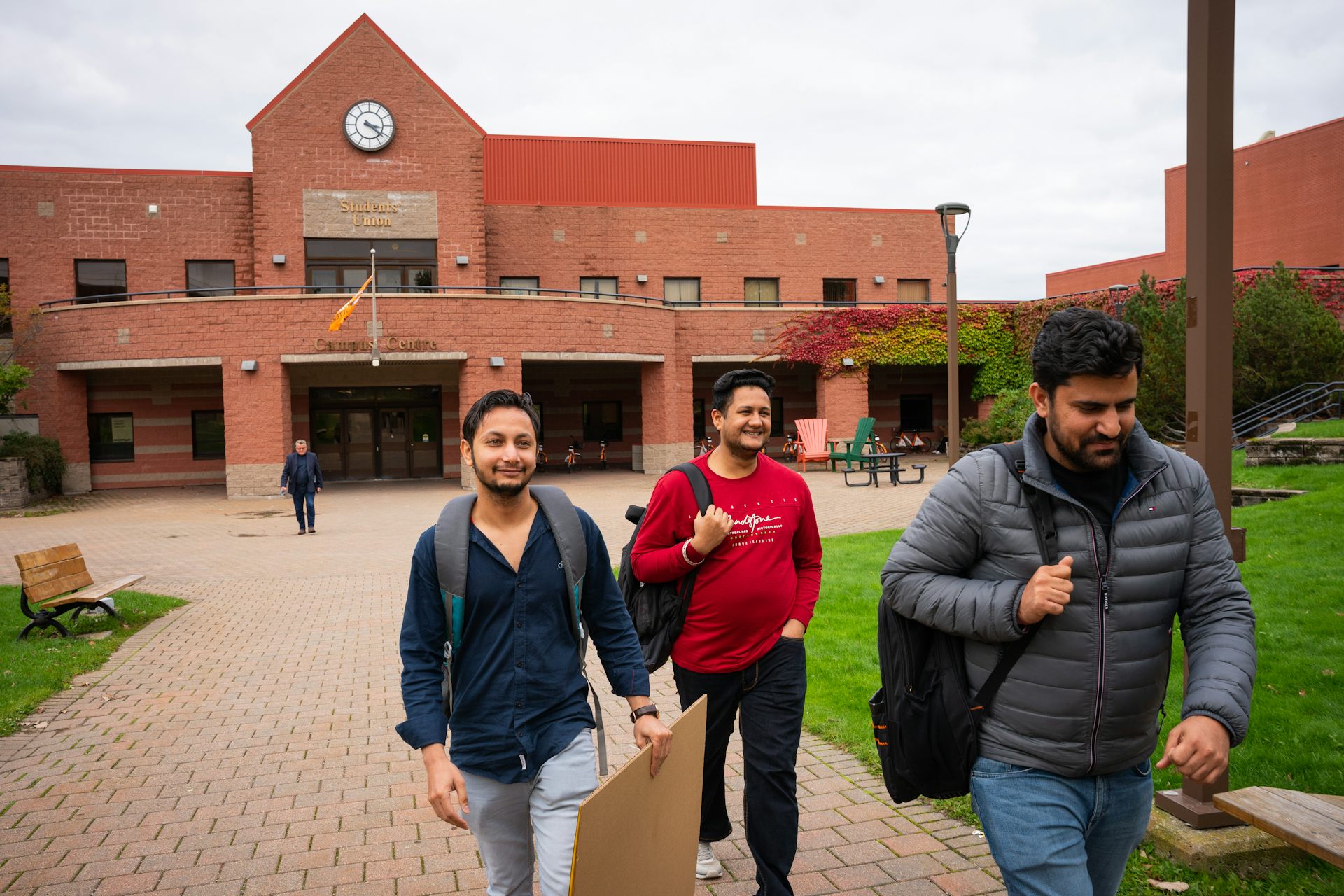 Three young men smile as they walk on a university campus.