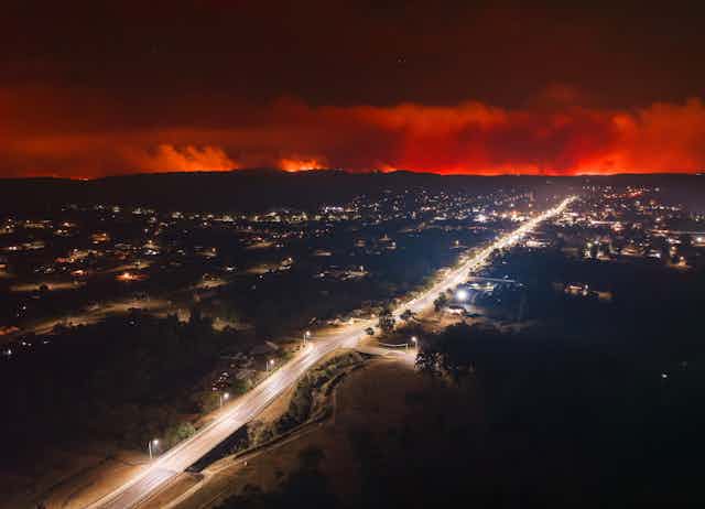 Aerial night view of town with bushfire on the horizon