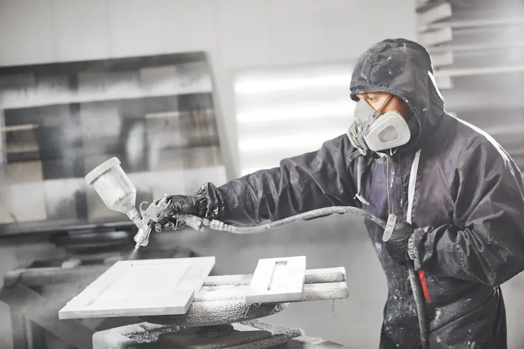 Man staining wood with white spray gun.