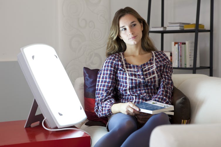Young woman reading by a therapy lamp