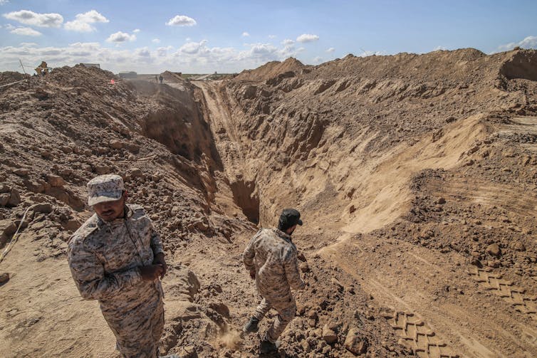 Men in camouflage uniforms look at a massive hole in the ground.