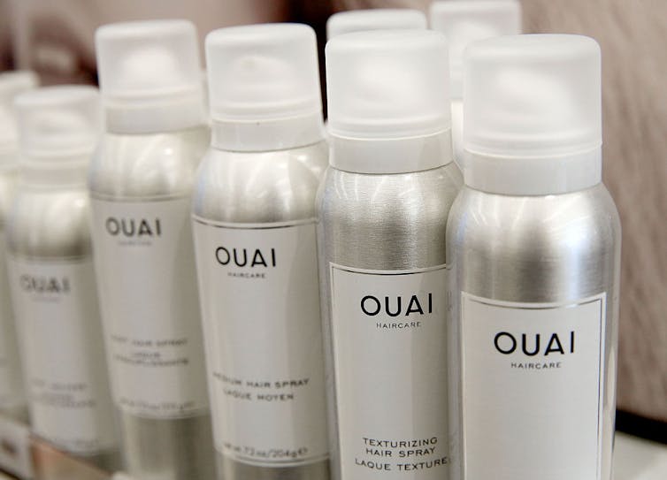 A row of silver bottles of hair spray with a white label and black text.