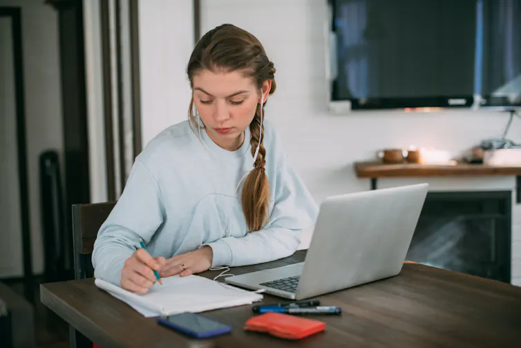 Une jeune femme qui suit un cours en ligne depuis son salon avec un ordinateur et des écouteurs