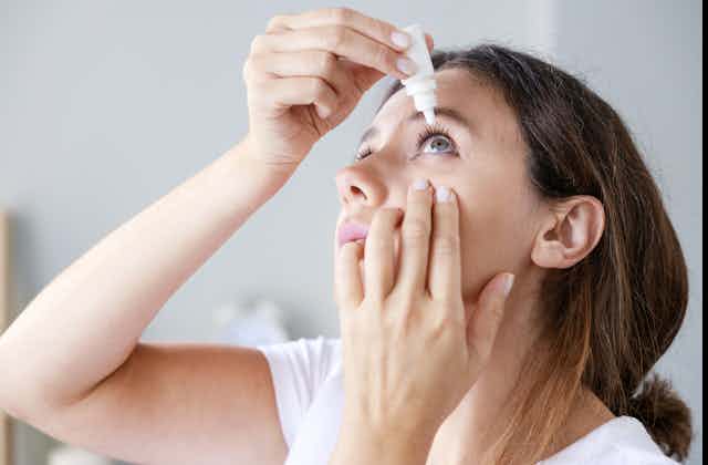 A young woman uses an eyedropper for her left eye.