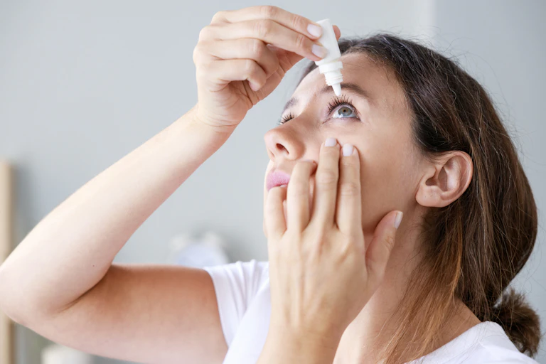 A young woman uses an eyedropper for her left eye.