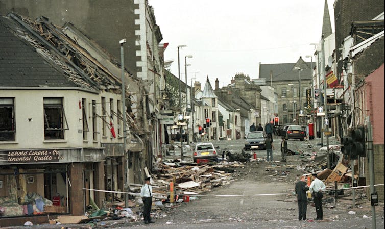 A photo of damaged buildings along a street. Debris lines the street.