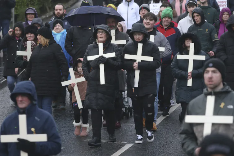 People in raincoasts carry crosses and walk along a road.