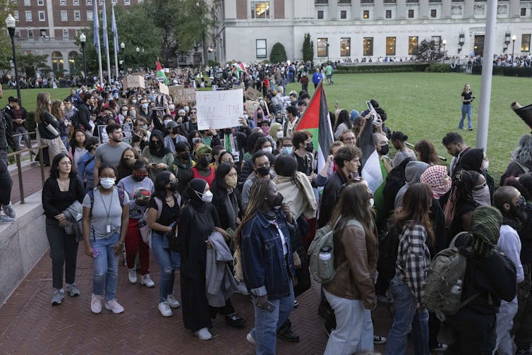 People seen at a demonstration in a university courtyard, some holding Palestinian flags, others with signs saying free Gaza and free Palestine.
