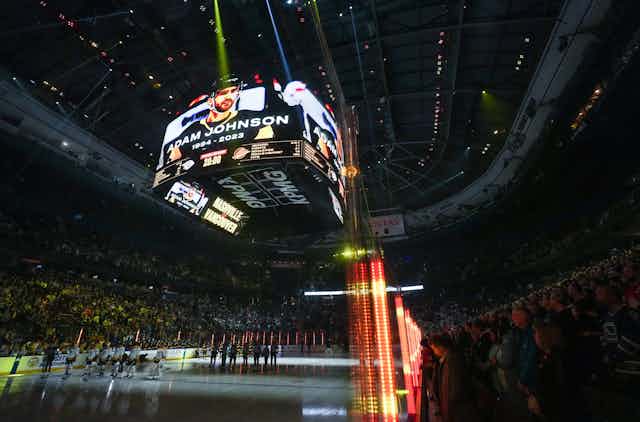 A photo of a hockey player is displayed on a giant screen cube in the middle of a hockey rink, along with the name 'Adam Johnson'
