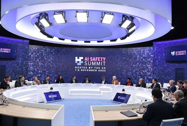A photo of dignitaries sitting around a conference table in front of a sign that reads 'AI SAFETY SUMMIT, HOSTED BY THE UK 1–2 NOVEMBER 2023"