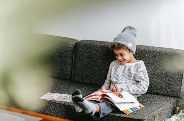 A young boy sits on a couch looking at a picture book