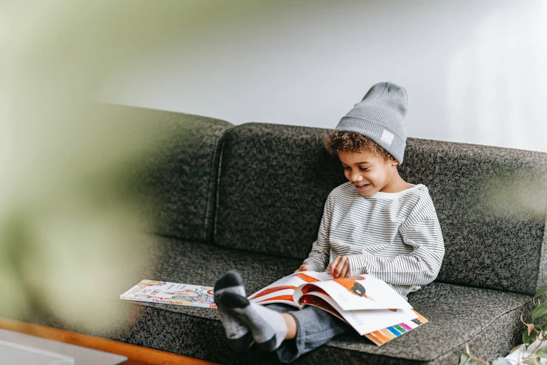 A young boy sits on a couch looking at a picture book