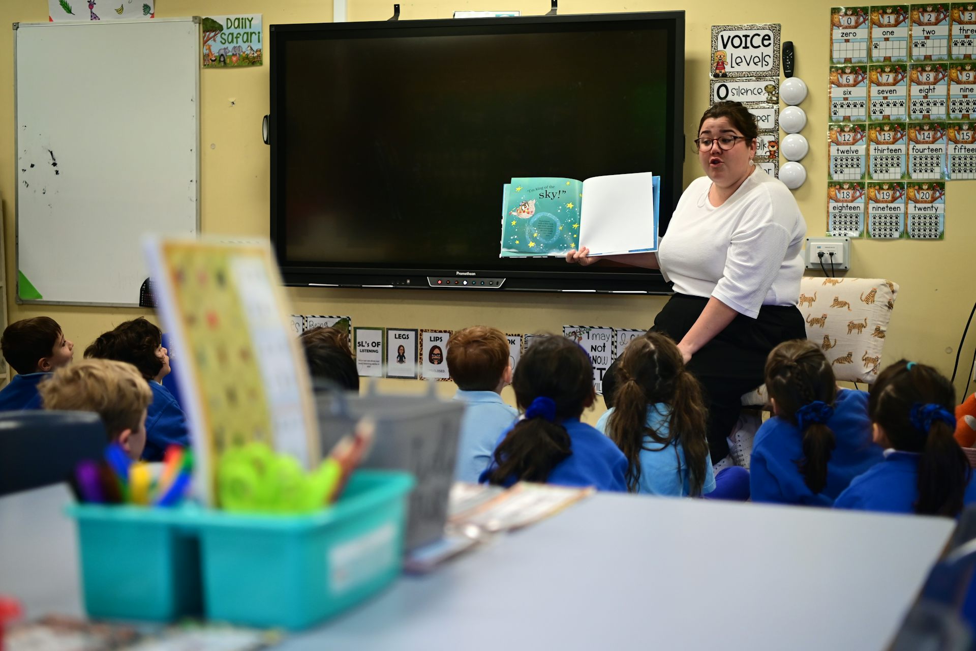 A teacher in a classroom reads to young students who are seated on the floor.