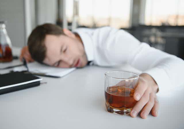 Drunk office worker asleep on his desk with drink in his hand