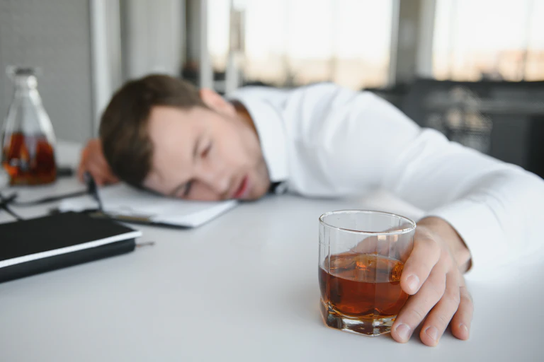 Drunk office worker asleep on his desk with drink in his hand