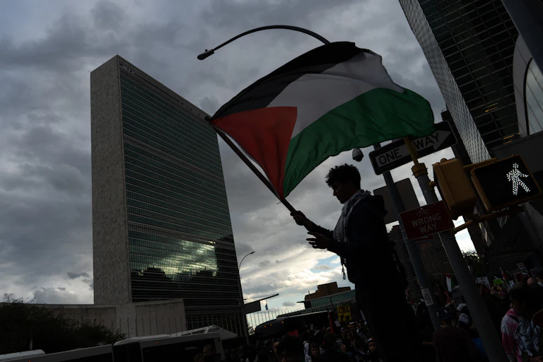 A person waves a Palestinian flag in front of a tall building.