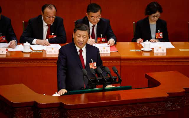 Xi Jinping speaks during the Closing Session of the National People's Congress with CCP officials taking notes behind him.