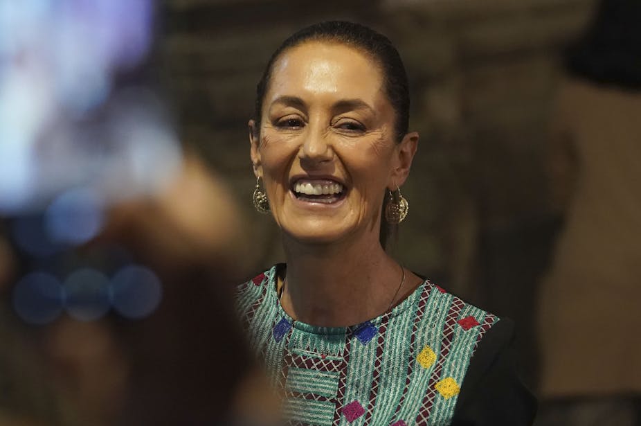 A woman in a colorful top and with loop earrings smiles.