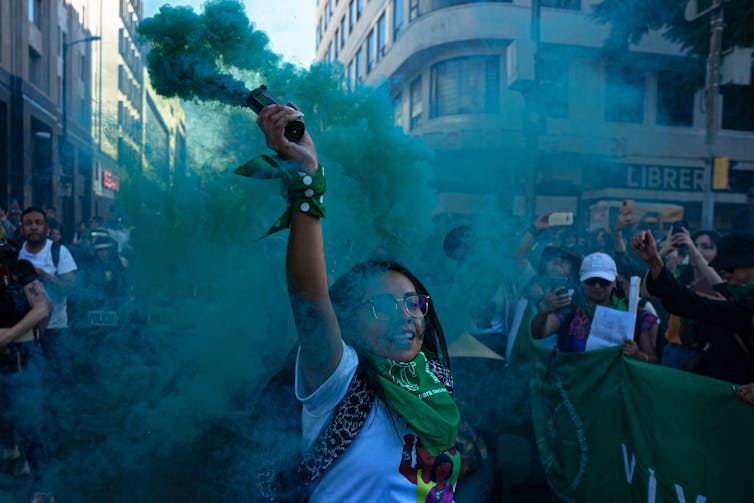 A woman holds a green flare during a street protest.