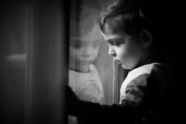 sad child looking through window in black and white photo