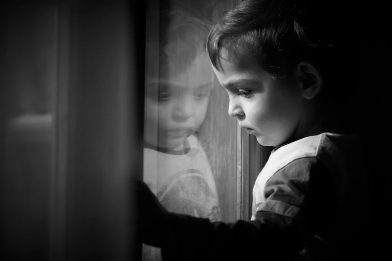 sad child looking through window in black and white photo