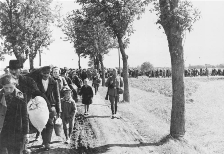 An archival black and white photograph of refugees marching.