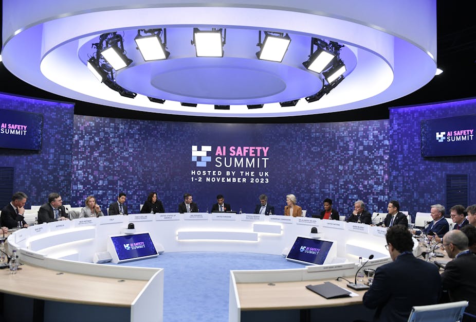 Une photo de dignitaires assis autour d'une table de conférence devant un panneau portant l'inscription suivante 'AI SAFETY SUMMIT, HOSTED BY THE UK 1–2 NOVEMBER 2023"