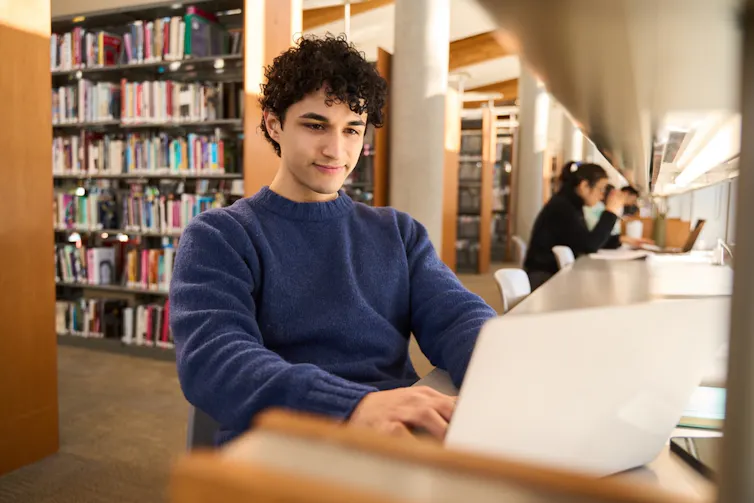 Un étudiant avec un ordinateur faisant des recherches en bibliothèque