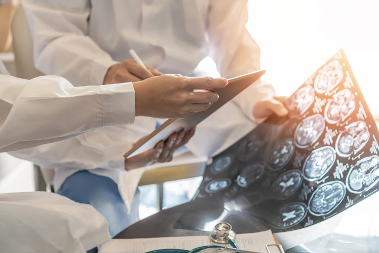 Two members of a medical team hold a tablet and pen and a sheet of brain images.