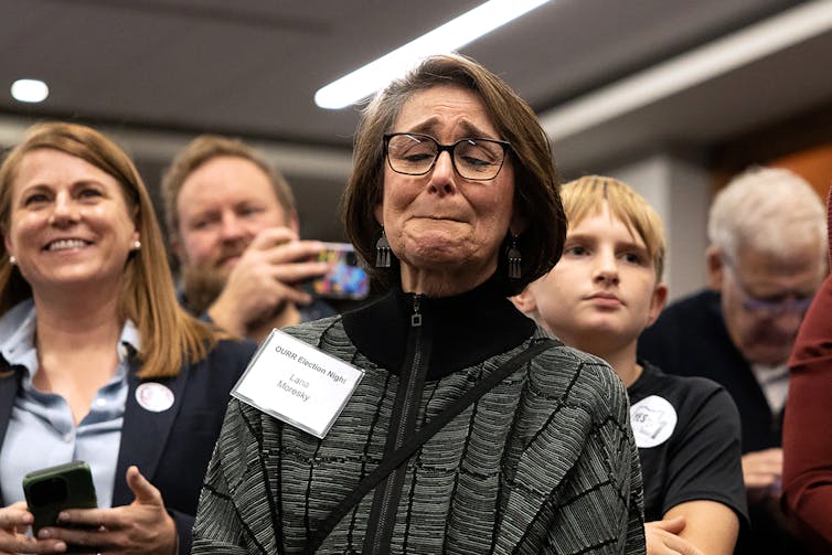 A woman closes her eyes and appears to be crying, surrounded by other people.