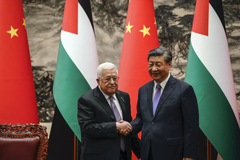 Two men shake hands in front of red, white, green and black flags.