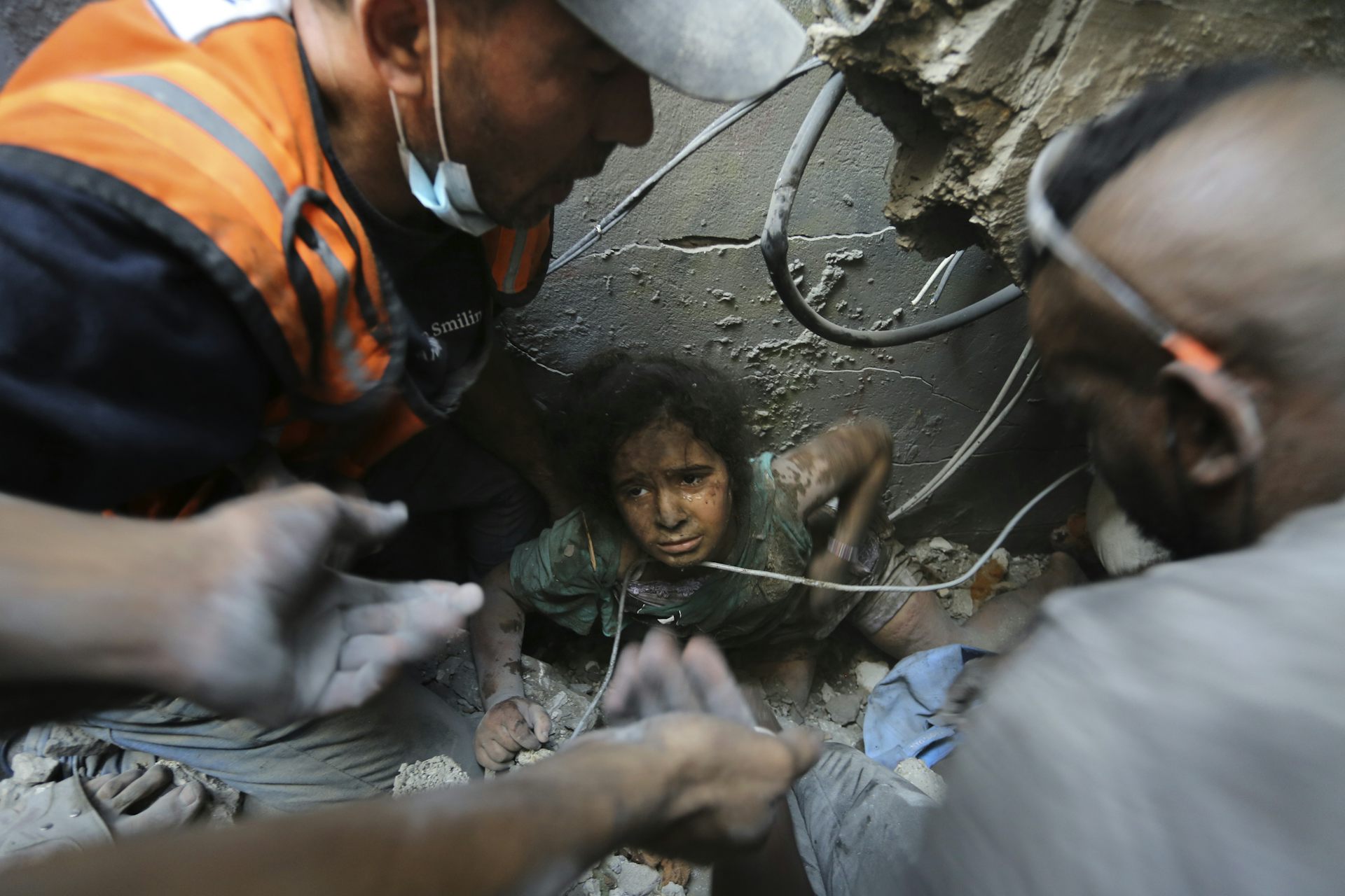 A young girl peers up from rubble as workers dig to free her.