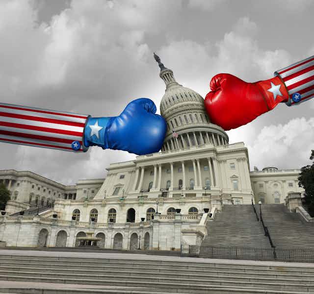 A blue boxing glove and a red boxing glove come from opposite sides of the US Capitol building, twisting the building's dome.