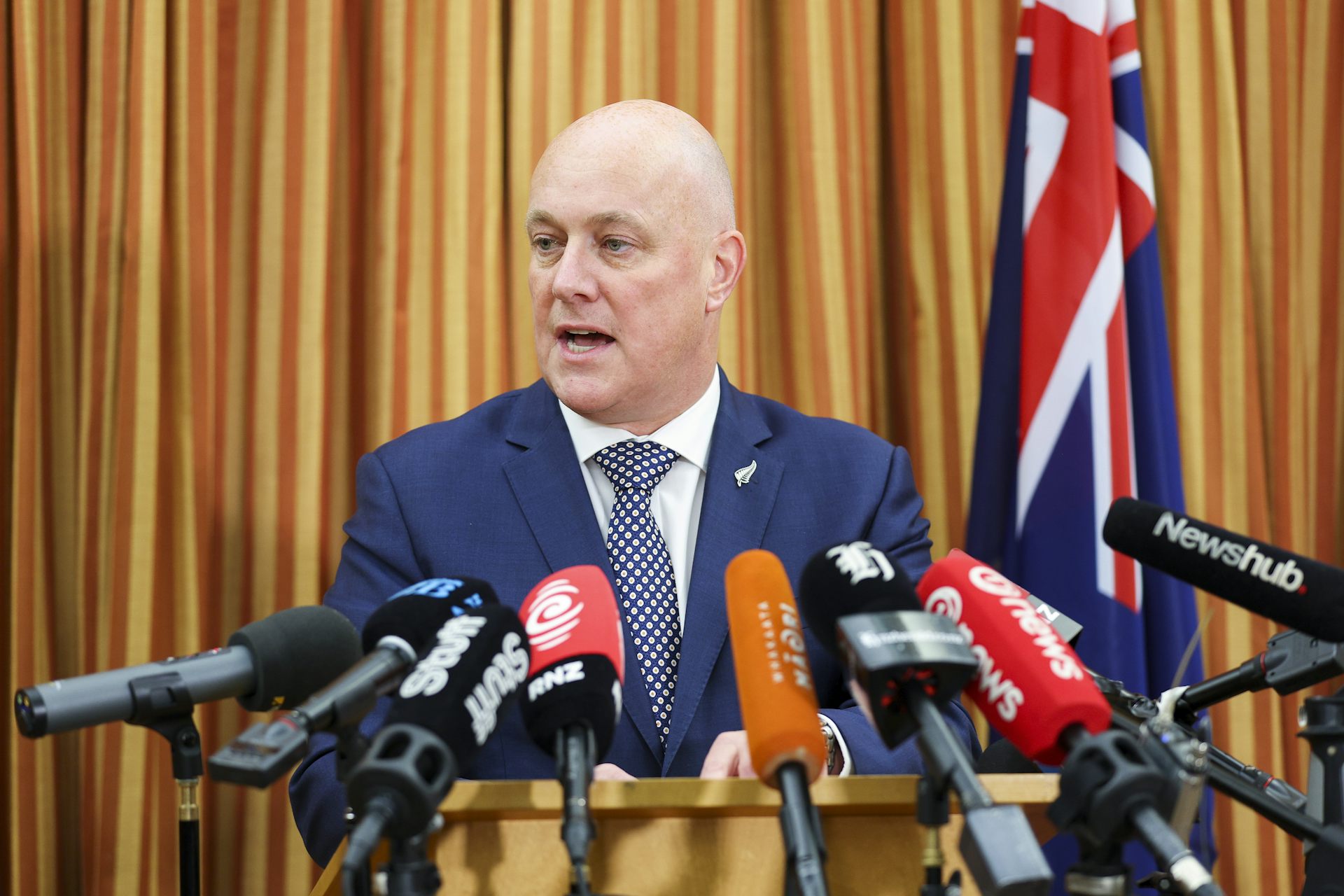 Christopher Luxon speaking into media microphones at press conference
